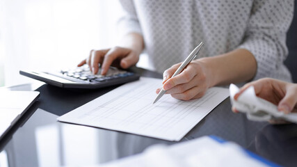 Woman accountant using a calculator and laptop computer while counting taxes with a client or colleague. Business audit team.