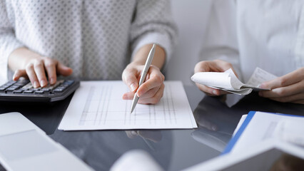 Woman accountant using a calculator and laptop computer while counting taxes with a client or...