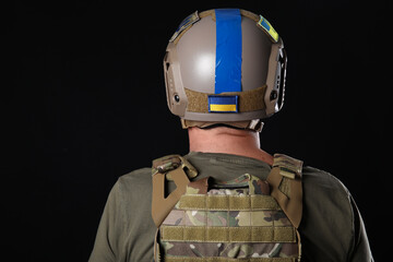 Ukrainian soldier with armor on dark background, back view