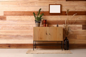 Chest of drawers with houseplant, drum and reed diffuser near wooden wall in room
