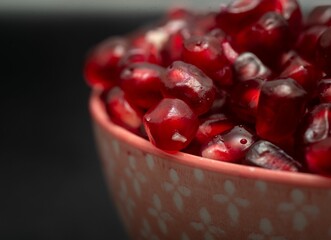 Macro shot of a bowl full of red pomegranate juicy seeds, on the black background