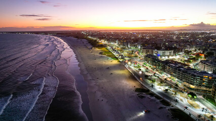 Vista de Drone sobre a praia e mar no pôr-do-sol em Cabo Frio Brasil, com a cidade iluminada. 