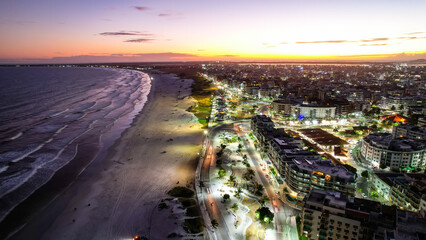 Fototapeta na wymiar Vista de Drone sobre a praia e mar no pôr-do-sol em Cabo Frio Brasil, com a cidade iluminada. 