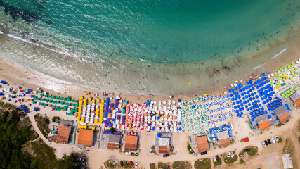 Drone view on the beach with sea and waves and white sand, tourists with umbrella
