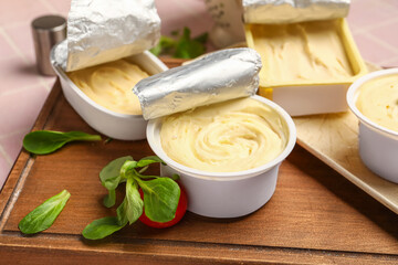 Wooden board with boxes of processed cheese and basil on pink tile background