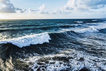 Scenic view of rough ocean waves crashing against beach on a cloudy day