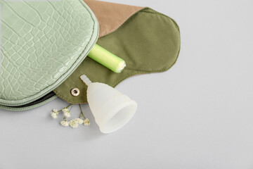 Lady's cosmetic bag with reusable menstrual pad, cup and tampon on grey background