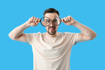 Naklejka premium Handsome man with magnifiers showing tongue on blue background