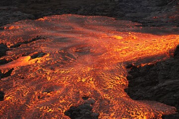 Volcanic eruption with glowing orange lava flow surrounded by a pool of bubbling magma