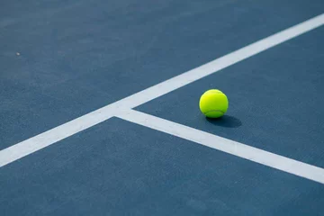 Landscape of a blue and green tennis court with a ball on it on a sunny day © Jwphotoworks/Wirestock Creators