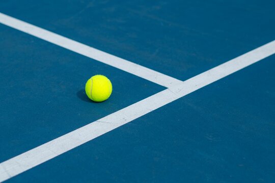 Landscape of a blue and green tennis court with a ball on it on a sunny day