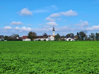 Large green field and parish Church of St. Vitus on a distance in Iffeldorf, Germany with blue sky