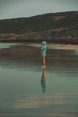 Naklejka premium Vertical shot of a female in a blue hoodie and shorts standing in the Woolacombe beach in July 2022