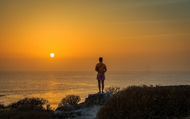 Silhouette of a male enjoying the view of the sea under a bright sunset sky