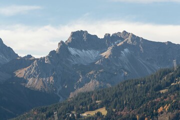 Aerial view of steep rocky mountains with green trees and forests under blue cloudy sky