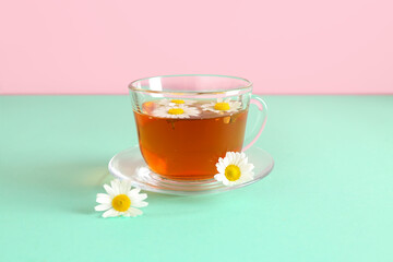 Cup of natural chamomile tea and flowers on turquoise table near pink wall