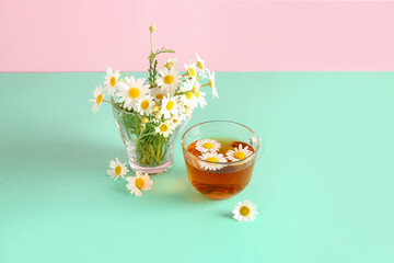 Cups of natural chamomile tea and flowers on turquoise table near pink wall