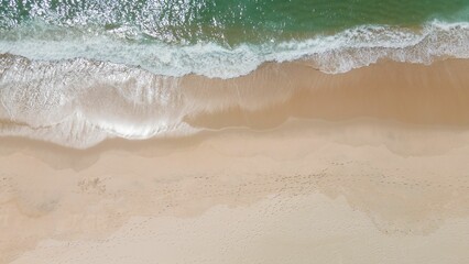 Aerial shot of ocean waves on a sandy beach in Portugal.