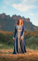 Fototapeta premium Beautiful smiling red-haired lady with a traditional blue dress decorated with goldwork in a field
