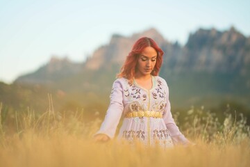 Beautiful red-haired lady with an embroidered white dress and gold belt in a sunny field in Spain
