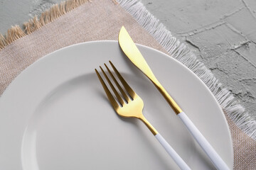 Plate with golden fork, knife and kitchen napkin on green grunge background