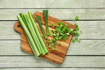 Board with slices of fresh leek on green wooden background