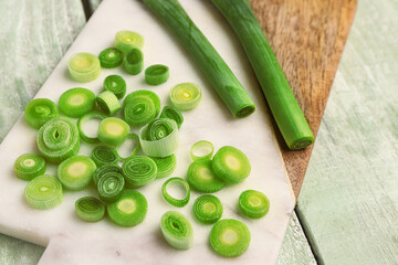 Board with slices of fresh leek on green wooden background