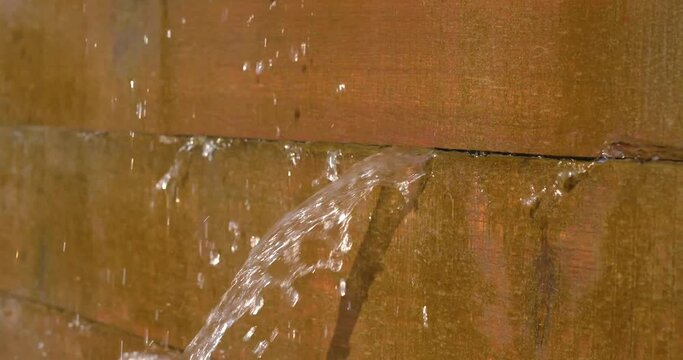 Slow motion close up of water leaking through a wood plank dam.

