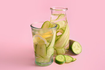 Glass and bottle of infused water with cucumber slices on pink background