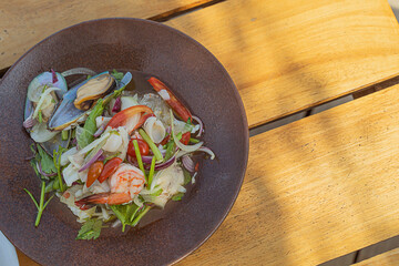 Spicy seafood salad, popular food on a wooden table, appetizing in a cafe next to the sea, Sue Flamingo, Ao Yon Beach, Phuket Thailand