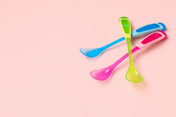 Different colorful spoons for baby on pink background