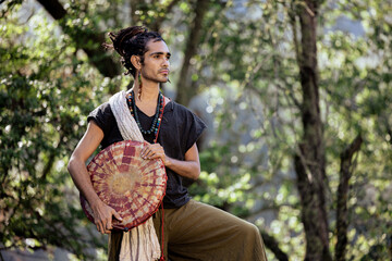 young mexican man with bohemian style with drum and nature background
