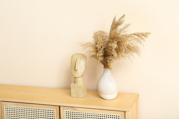 Wooden chest of drawers with pampas grass and decor near beige wall in room