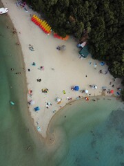 Aerial shot of the people resting on the beach and swimming in the blue sea on a sunny day