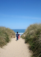 Young Girls running through sand dunes toward the ocean