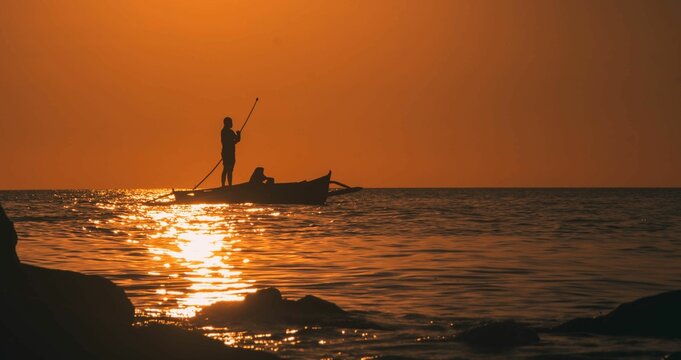 Image of a boat with a person on it in the sea during golden hour