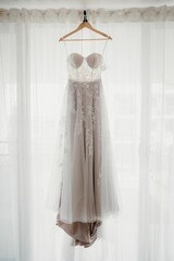 White bridal dress hanging from the wall near the window