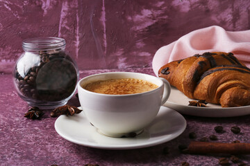 Cup of delicious espresso with coffee beans and croissant on purple background, closeup