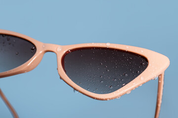 Stylish beige sunglasses on blue background, closeup