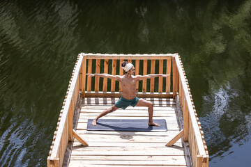 young and handsome dark-skinned mexican latino man with bohemian style practicing yoga on dock with lake in background