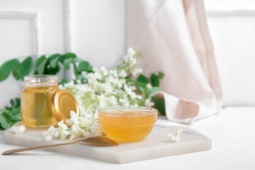 Fototapeta na wymiar Jar and bowl of honey with flowers of acacia on light background