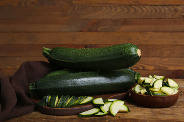 Board with fresh green zucchini and bowl of slices on wooden table