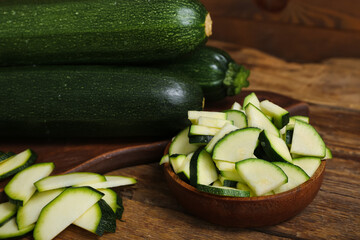Board with fresh green zucchini and bowl of slices on wooden table