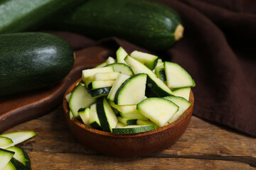 Board with fresh green zucchini and bowl of slices on wooden table