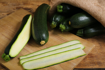 Sack bag with many fresh zucchini and board of slices on wooden background