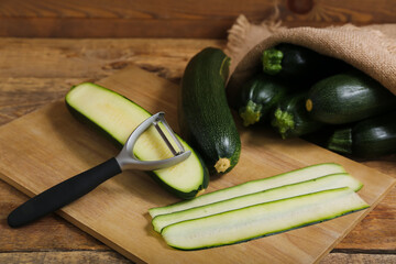 Sack bag with many fresh zucchini and board of slices on wooden background