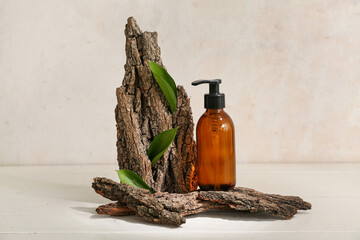 Composition with bottle of cosmetic product, tree bark and plant leaves on light background