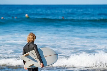 Person standing at the shore of the sea with splashing waves with a surfing board