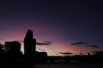 Silhouette of city buildings along the River Thames against a pink, dusk sky in London