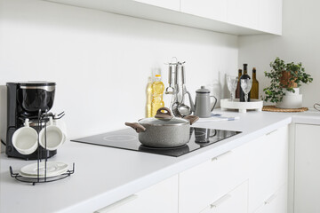 White countertop with electric stove, cooking pot and kitchenware